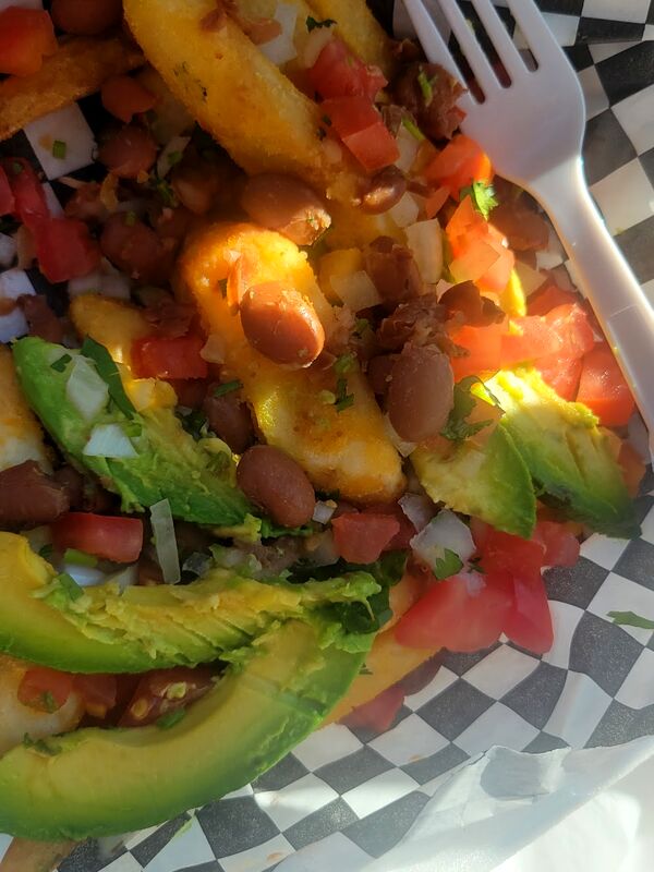 Asada fries in a checkered basket with avocado and tomato